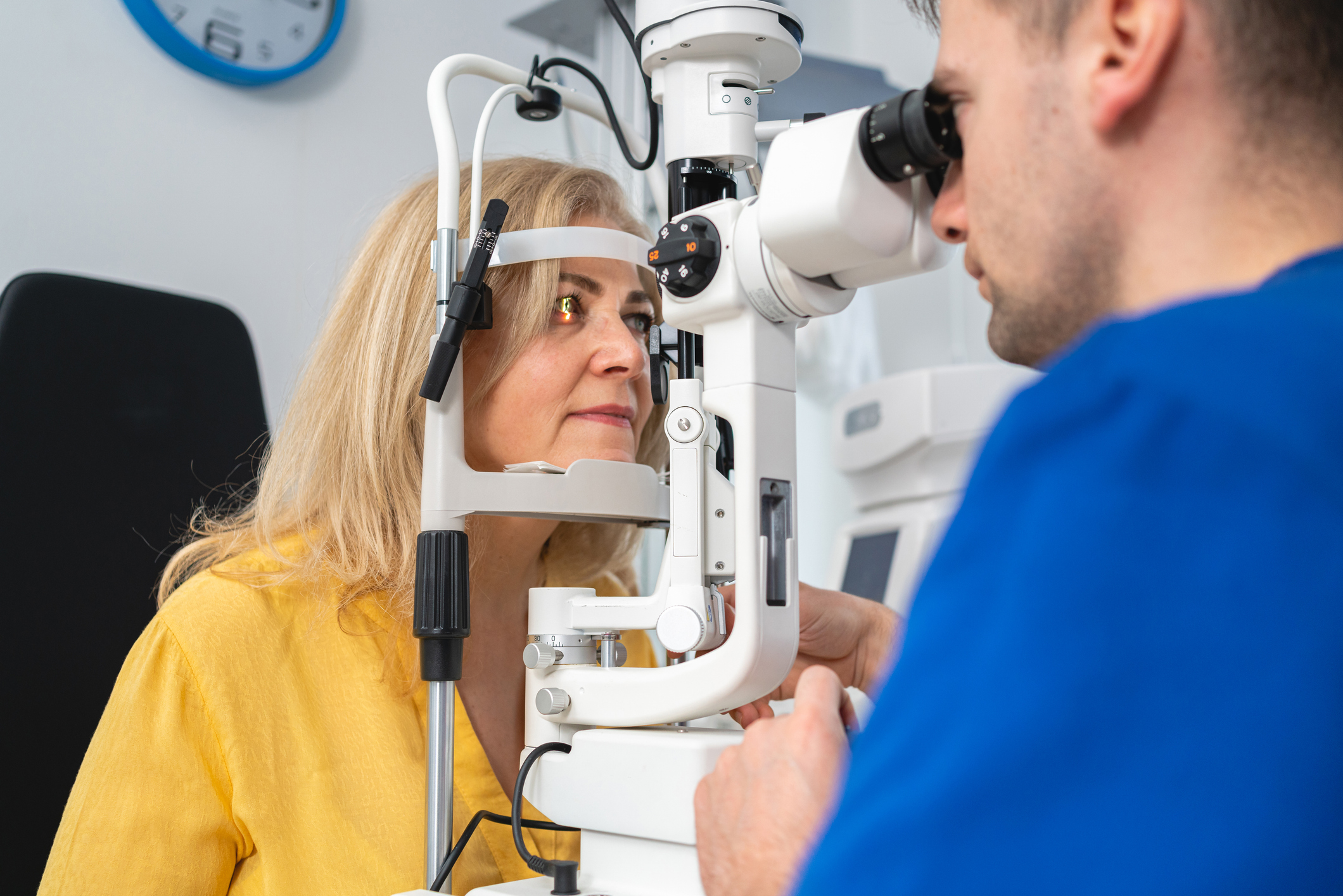 Caucasian male ophthalmologist examining with slit lamp structures of the eye, such as the cornea, iris, and lens, on a senior female patient at the ophthalmology clinic