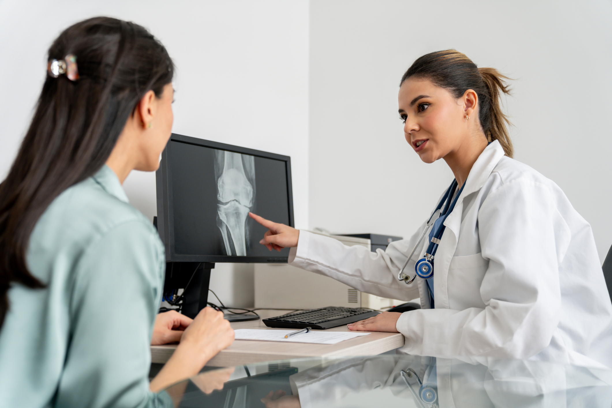 Latin American doctor in her office looking at a knee x-ray with a patient using the computer - orthopedics concepts