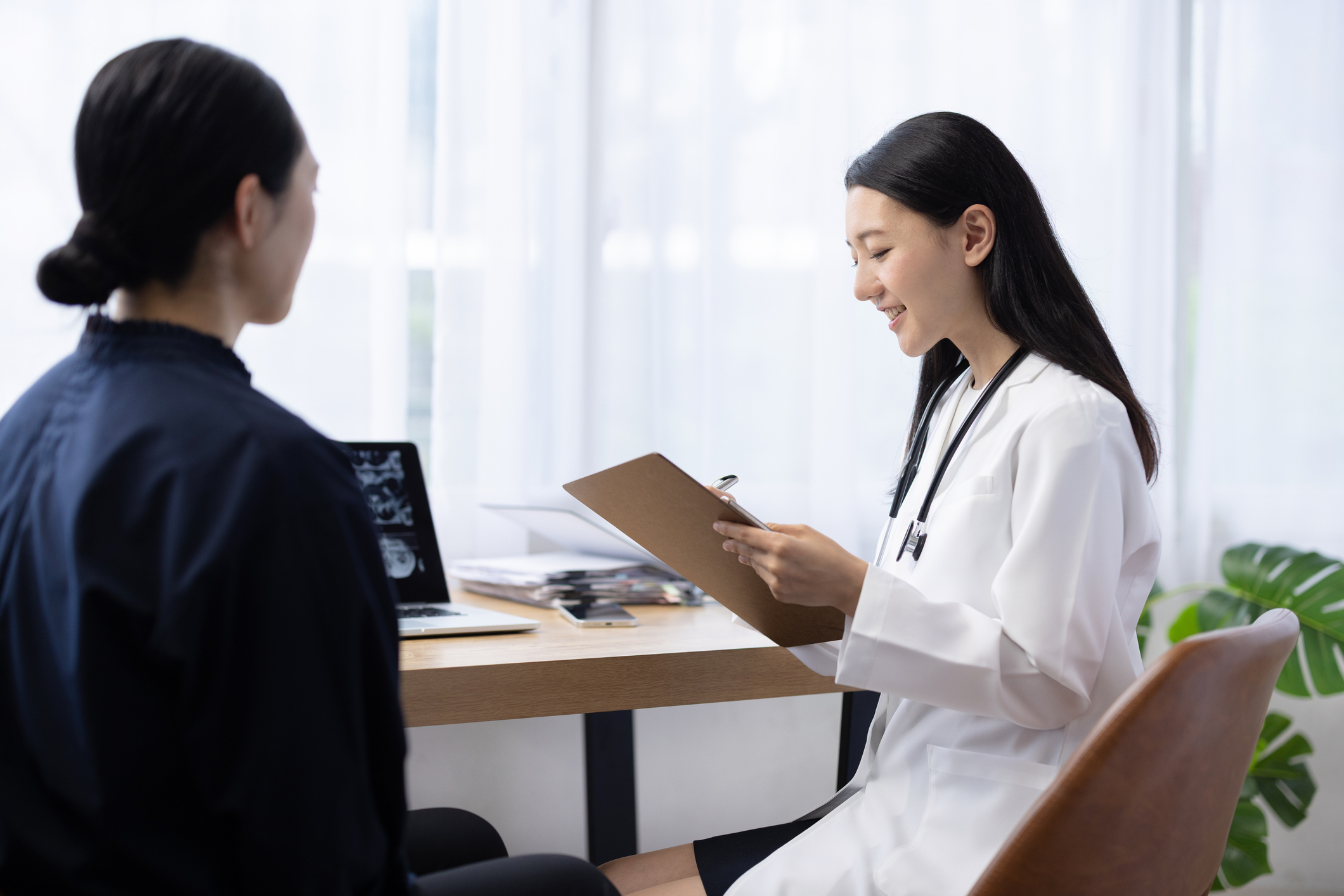 Young Japanese female doctor writing on medical chart during patient examination